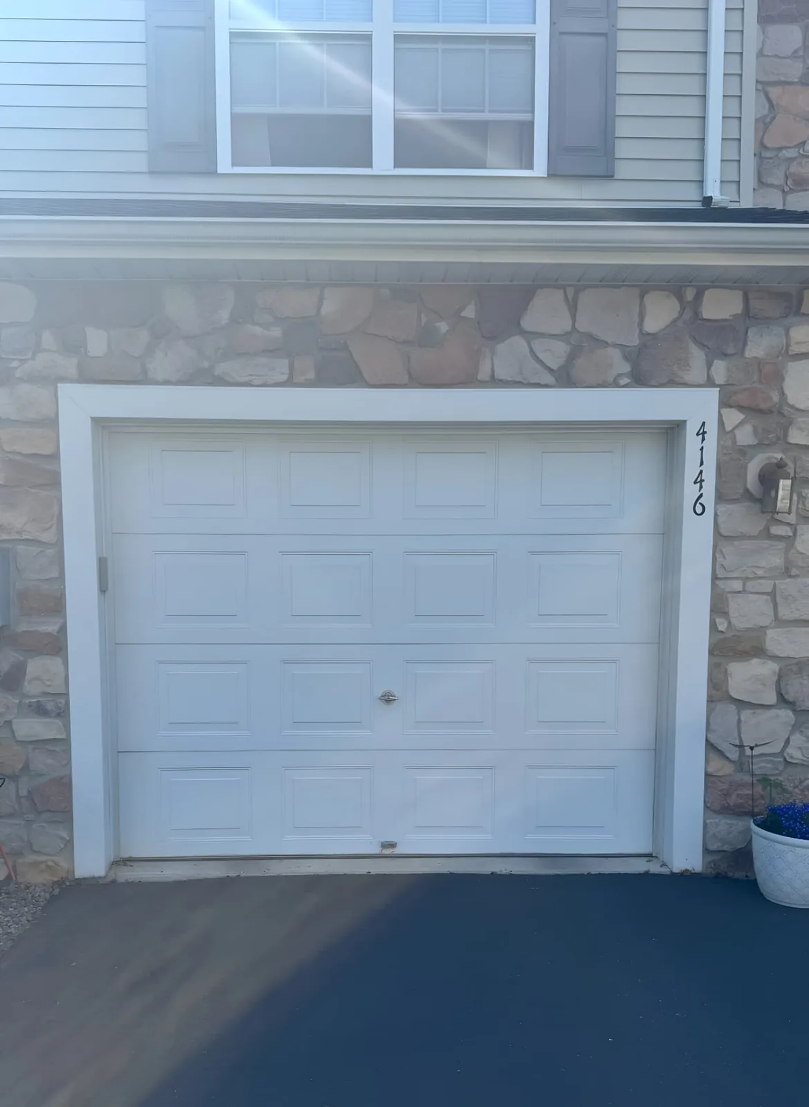 White raised-panel single garage door framed by stone masonry and white trim