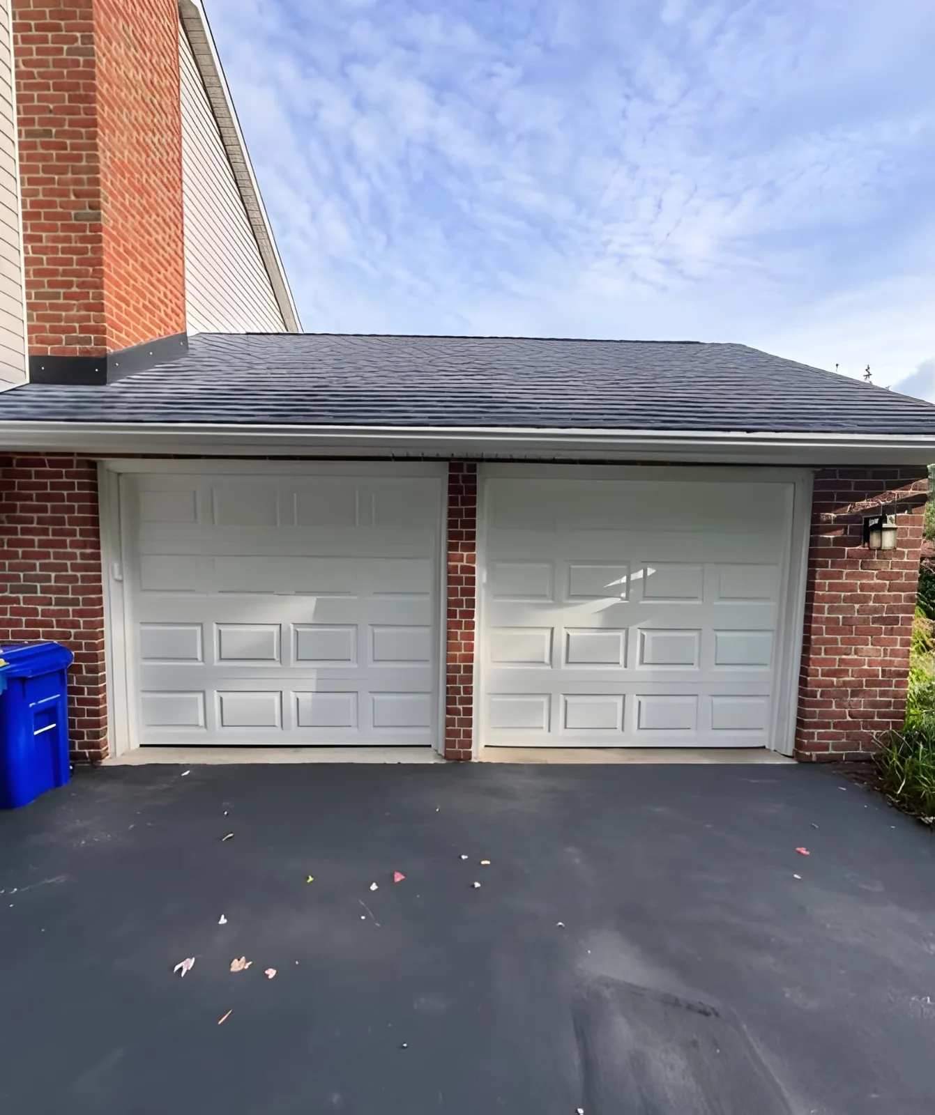 Two white raised-panel garage doors installed on a red-brick residential garage