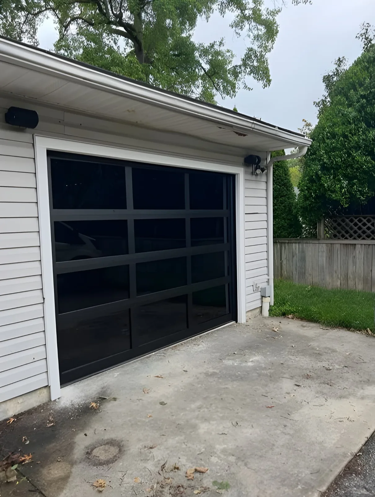 Modern black full-view glass garage door installed on a white detached garage