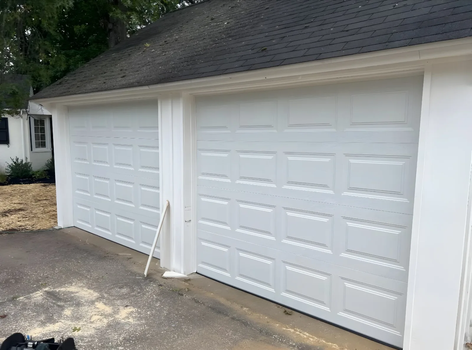 Two wide white raised-panel garage doors installed on a detached garage